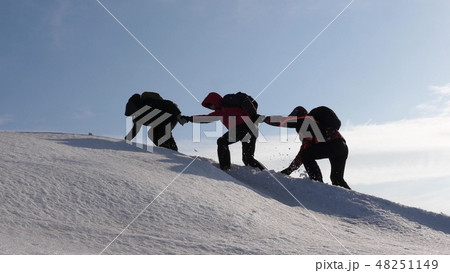 climbers hand in hand climb to top of a snowy mountain. the team of travelers in winter go to their climbers hand in hand climb to top of a snowy mountain. the team of travelers in winter go to their 48251149