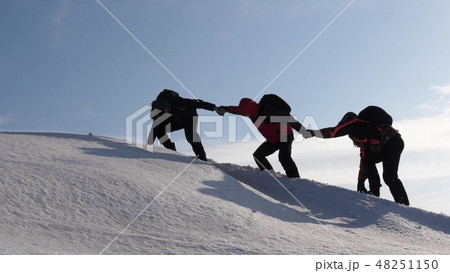 climbers hand in hand climb to top of a snowy mountain. the team of travelers in winter go to their 48251150
