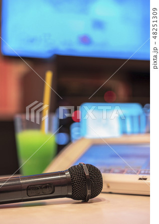 カラオケクラブの黒いマイクロフォン、リモコン、メロンソーダのドリンクとテレビスクリーン。 48251309
