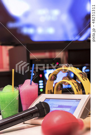 カラオケクラブの黒いマイクロフォン、リモコン、メロンとストロベリーソーダのドリンクと黄色いタンバリン 48251311