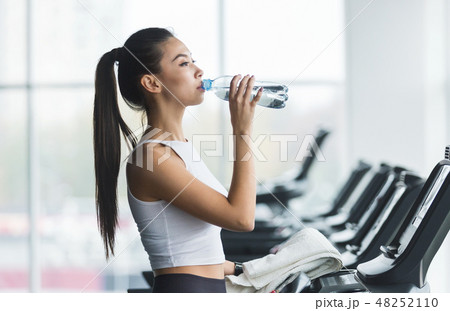 Woman drinking water after exercising on treadmill Woman drinking water after exercising on treadmill 48252110