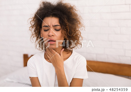 African-american woman with sore throat sitting on bed African-american woman with sore throat sitting on bed 48254359