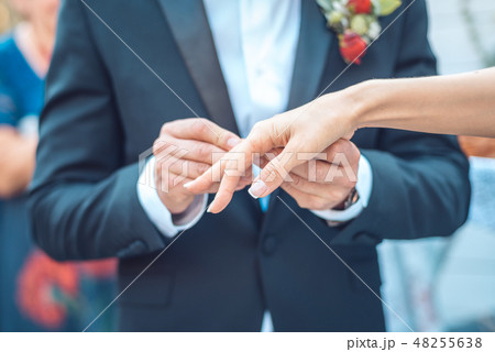 Groom In a dark blue jacket with a boutonniere puts a ring on the bride's hand. close-up shot of 48255638
