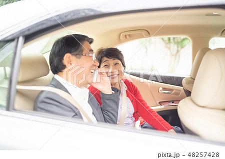高級車の後部座席で宿泊先の情報をスマートフォンで楽しそうに話す笑顔の熟年老夫婦 48257428