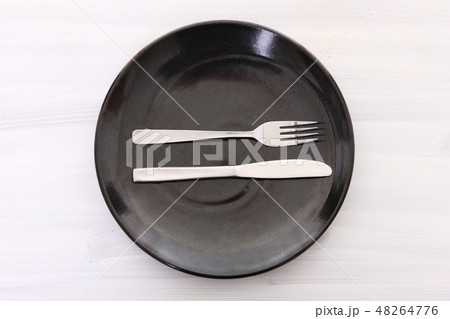 白い木製テーブルに置かれた黒い皿とカトラリーによる大満足の合図 48264776