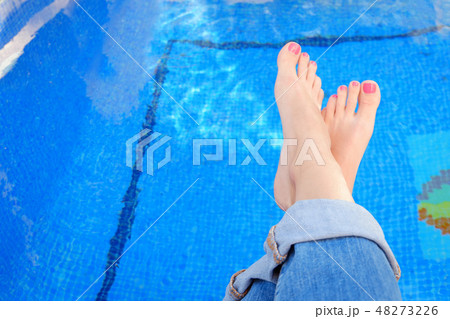 Crossed woman feet in blue jeans by swimming pool 48273226