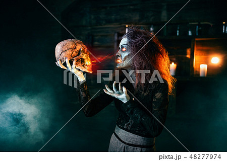 Scary witch holds human skull and reads the spell 48277974