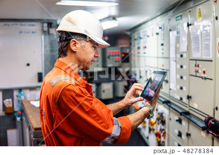 Marine chief engineer watching digital tablet in engine control room 48278384
