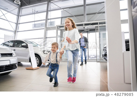 Kids running and laughing in salon with automobiles. 48279085