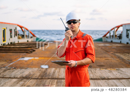 Deck Officer on deck of offshore vessel holds VHF walkie-talkie radio Deck Officer on deck of offshore vessel holds VHF walkie-talkie radio 48280384