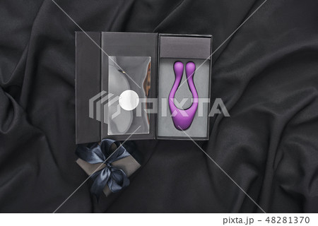 Unique design. Close up of purple sex toy for her and black gift box on a black silk fabric 48281370