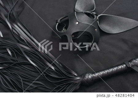 Impress him. Top view of bdsm leather kit (black whip and mask) against of a black silk. Impress him. Top view of bdsm leather kit (black whip and mask) against of a black silk. 48281404