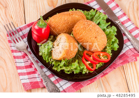 three fried breaded cutlet with lettuce on a black plate and wooden background three fried breaded cutlet with lettuce on a black plate and wooden background 48285495