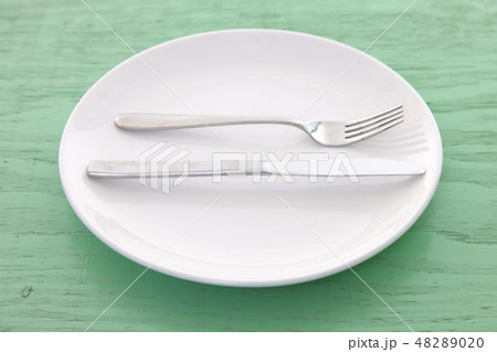 緑の木製テーブルに置かれた白い皿とカトラリーによる大満足の合図 48289020