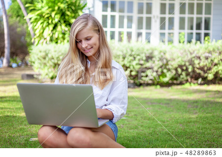 Beautiful blonde girl with a laptop on a green lawn, education and distant work 48289863