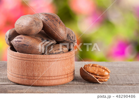 pecan nuts in a wooden bowl on the old board with blurred garden background 48290486