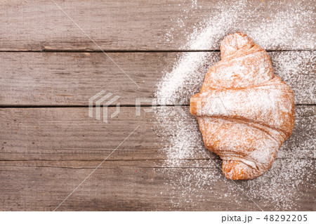 one croissant sprinkled with powdered sugar on old wooden background with copy space for your text one croissant sprinkled with powdered sugar on old wooden background with copy space for your text 48292205