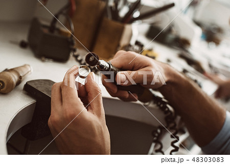 On the way to perfection. Close-up of male jeweler's hands polishing silver ring at his jewelry 48303083