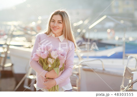 Beautiful girl in spring or autumn, by the sea in the boat Bay. With a bouquet of flowers in his 48303555