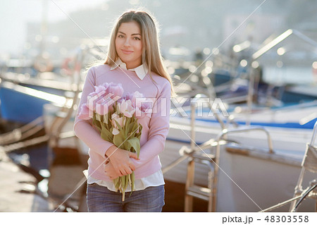Beautiful girl in spring or autumn, by the sea in the boat Bay. With a bouquet of flowers in his 48303558