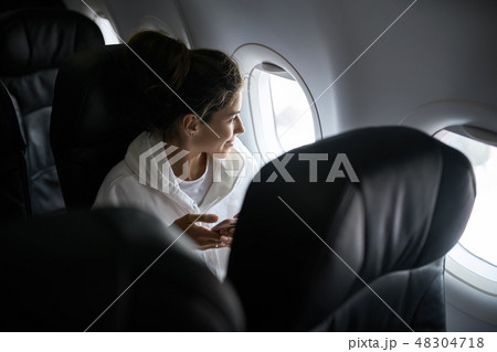 Woman with smartphone sits on black seat in plane Woman with smartphone sits on black seat in plane 48304718