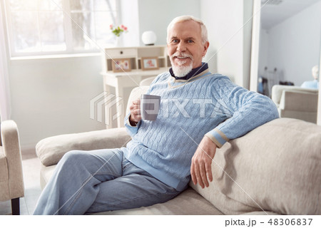 Joyful elderly man posing with coffee cup on sofa 48306837