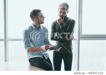 Two focused male co-workers deep in discussion together, while standing in a modern office 48307132