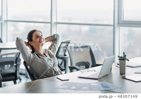 Happy businesswoman relaxing with hands behind head at office desk. Daydreaming concept Happy businesswoman relaxing with hands behind head at office desk. Daydreaming concept 48307149
