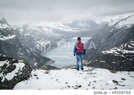 Man traveller with backpack standing back on edge and looking at scenery mountain landscape under 48308768