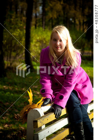 Young blonde woman in violet coat in park Young blonde woman in violet coat in park 48308777