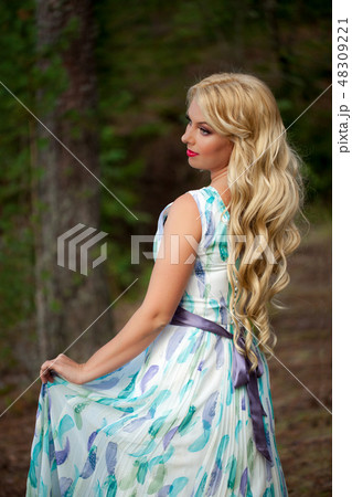 Young beautiful blonde woman in white dress with blue and green flowers posing in forest 48309221
