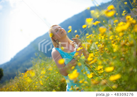 Young beautiful blonde girl in a chamomile field stands posing with a flower in her hands 48309276
