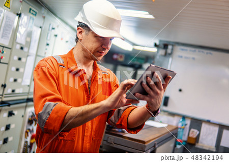 Marine chief engineer watching digital tablet in engine control room 48342194