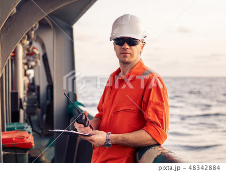 Deck Officer on deck of offshore vessel holds VHF walkie-talkie radio 48342884