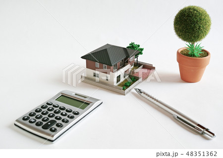 白い紙の上にあるミニチュアの家と電卓とボールペンと作り物の丸い鉢植えの木 48351362