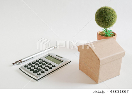 白い紙の上にあるボール紙の家と電卓とボールペンと作り物の丸い鉢植えの木 白い紙の上にあるボール紙の家と電卓とボールペンと作り物の丸い鉢植えの木 48351367