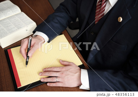 リーガルパッドにメモをする男性弁護士の手元・バッジあり 48356113