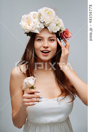 Beautiful young girl smiling and posing with flowers on gray background. 48356778