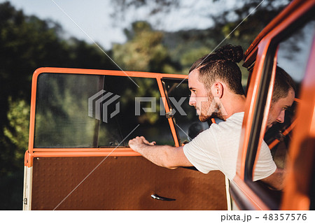 A young man getting out of a car on a roadtrip through countryside. 48357576