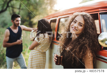 A group of friends standing outdoors on a roadtrip through countryside, holding bottles. 48357578