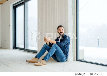 A mature man with cup of coffee sitting on the floor, furnishing new house. 48357636