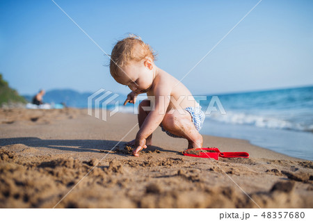 A small toddler girl sitting on beach on summer holiday, playing. 48357680