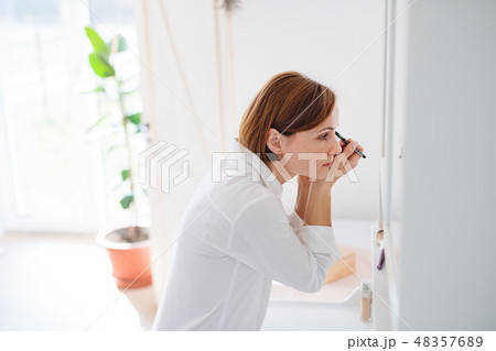 A young woman putting on a make-up in the morning in a bathroom. 48357689