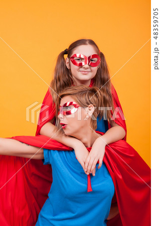 Beautiful mother and her cute little girl dressed like heroins playing together over yellow 48359705