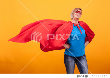 Young and beautiful blonde woman dressed like superheroine with red cape in the air. 48359732