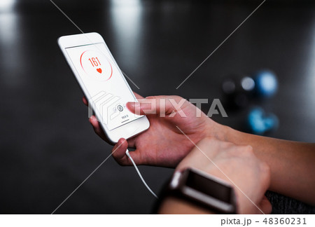 A midsection of woman with smartphone in a gym, checking heart rate. A midsection of woman with smartphone in a gym, checking heart rate. 48360231