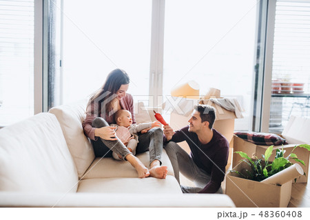 A portrait of young couple with a baby and cardboard boxes moving in a new home. A portrait of young couple with a baby and cardboard boxes moving in a new home. 48360408