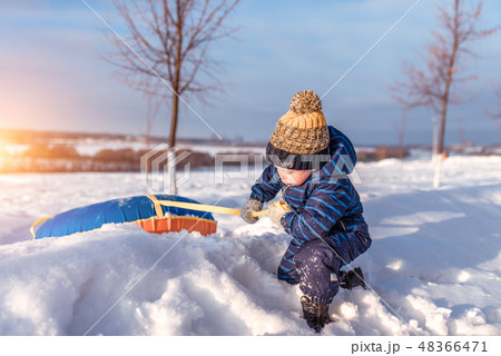 A little boy, 2-3 years old, dragging winter toy, pulling from snow-covered snowdrift from hill park A little boy, 2-3 years old, dragging winter toy, pulling from snow-covered snowdrift from hill park 48366471