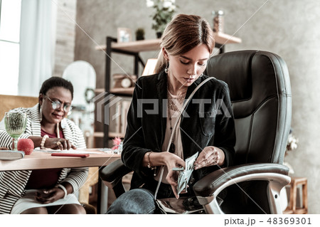 Young long-haired young woman in a black jacket taking money out of the wallet 48369301