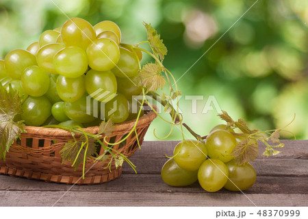 green grapes in a wicker basket on wooden table with blurred background green grapes in a wicker basket on wooden table with blurred background 48370999